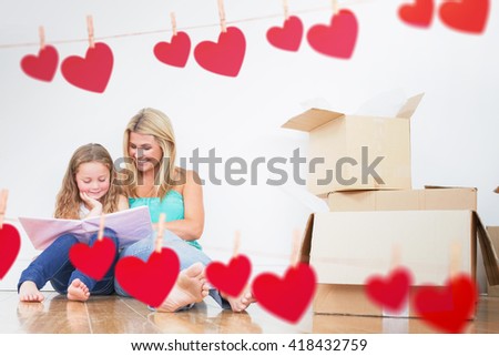 Mother and daughter reading a book against hearts hanging on a line