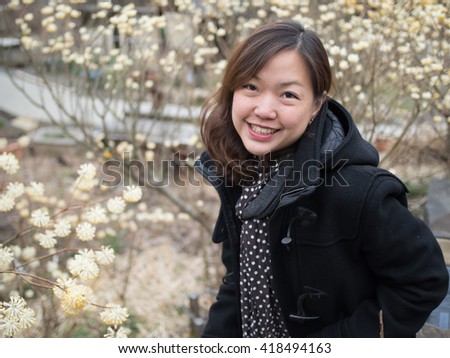 Asian women portrait - Asian female in black jacket looking and smiling to the camera. Background is yellow flower.