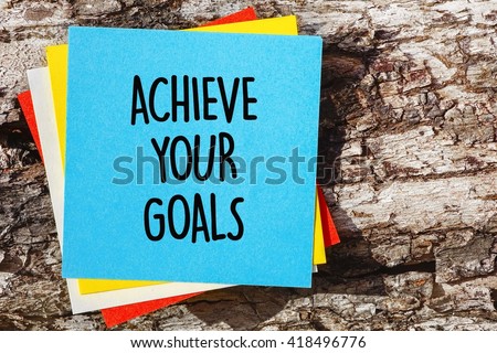 Word quotes of ACHIEVE YOUR GOALS on colorful memo papers with wooden background.