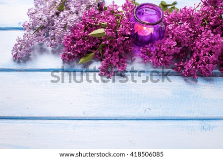 Fresh aromatic lilac flowers and candle on blue wooden background. Selective focus. Place for text.