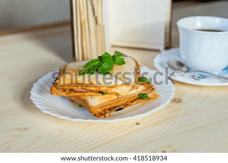 Homemade sandwich on white plate with coffee, notepad, spoon on wooden table