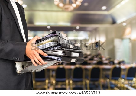Businessman is holding many document folders on Abstract blurred photo of conference hall or seminar room background, business busy concept