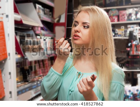 Portrait of smiling young blondie selecting lip gloss in store Royalty-Free Stock Photo #418527862