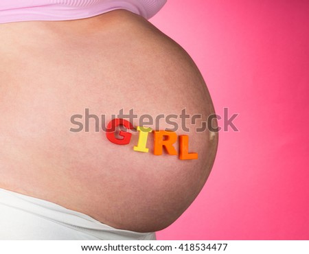 Belly of a pregnant woman with the word GIRL on a pink background.