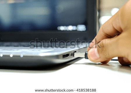 asian hand inserting black USB cable into laptop
