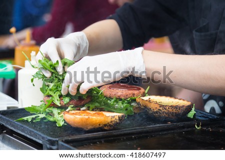 Chef making beef burgers outdoor on open kitchen international food festival event. Street food ready to serve on a food stall. Royalty-Free Stock Photo #418607497
