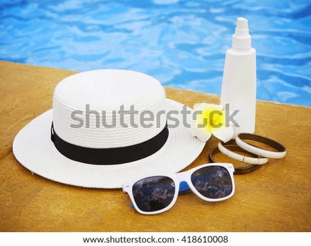 Suncream, sunglasses, hat, bracelet near the swimming pool. Vacation concept