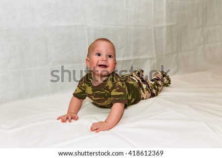 The Little boy in camouflage clothes lies on a white background