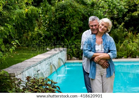 Portrait of loving senior man embracing wife from behind while standing at poolside