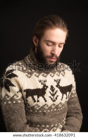 Studio shot of bearded young man in sweater looking down against of black background