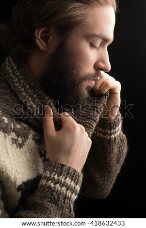 Handsome bearded man with eyes closed holding his sweater neck