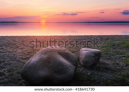 Beautiful landscape with stones on lake beach over sunset