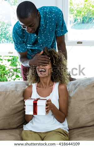 Man covering eyes of a woman while giving her a surprise gift