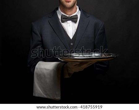 Waiter in black suit holding tray over black background. Royalty-Free Stock Photo #418755919