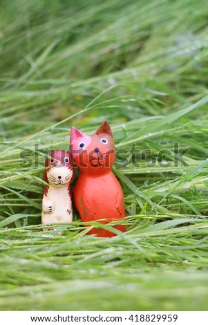 Wooden cat & puppy are sitting tenderly in the rainy grass.