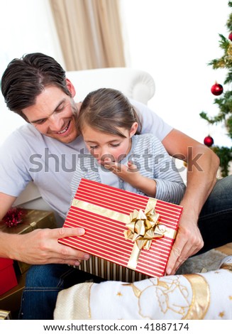 Surprised little daughter opening a Christmas present with her father at home