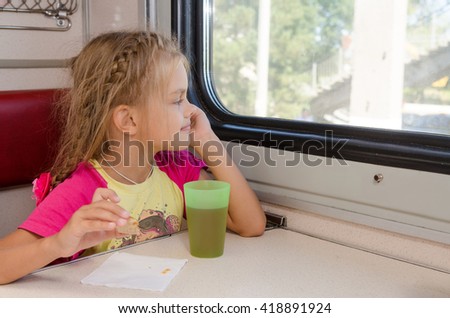 Six-year girl sitting on the train at the table on outboard second-class carriage and enthusiastically looking out the window