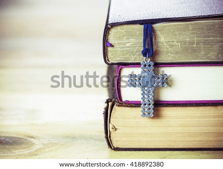 the metal cross hang on stack on old books  on the wooden table, Vintage color