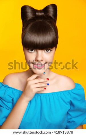 Beautiful smiling teen girl with bow hairstyle, makeup and colourful manicured polish nails. Funny girl in blue dress showing manicure fingers isolated on studio yellow background.