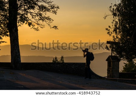 Man taking photo of sunset against Tuscany hills on the background. An unrecognizable person making pictures of sunset, sunrise against mountains on the background.  Silhouette, backlit