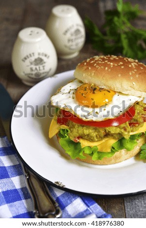 Vegetarian burger with guacamole and roasted egg on a vintage plate on a wooden background.