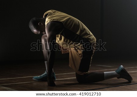 Basketball player preparing to play with knee on the floor and head lowered on a gym