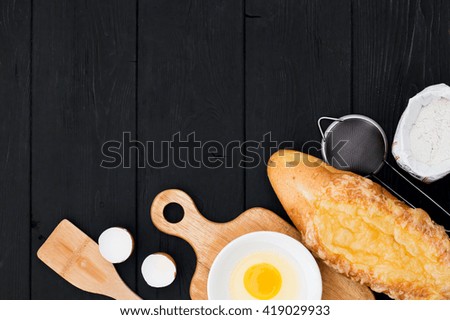 Ready to bake buns, bread. On black wooden background lie the ingredients and utensils.   Place for title