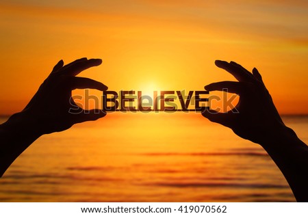 Silhouette, Close up Hand holding BELIEVE text with blurred sea sunset. sunlight effect. Royalty-Free Stock Photo #419070562