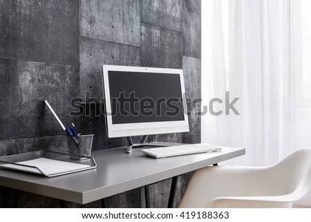 Minimalist computer desk with metal wire penholder and paper tray standing by a grey wall decorated in post industrial tiles  Royalty-Free Stock Photo #419188363