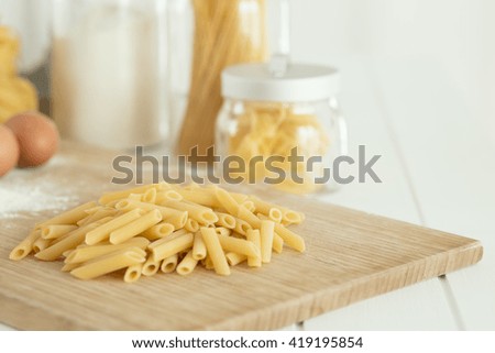 Uncooked dried penne over cutting board with flu and, eggs.
