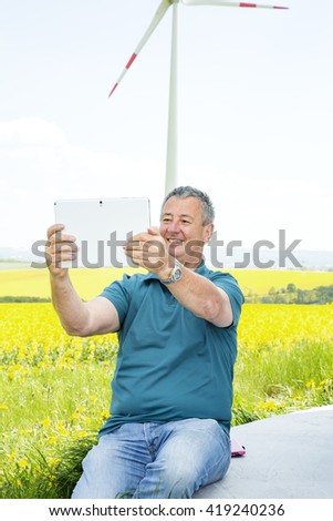 Man with tablet PC on the canola field with wind turbine