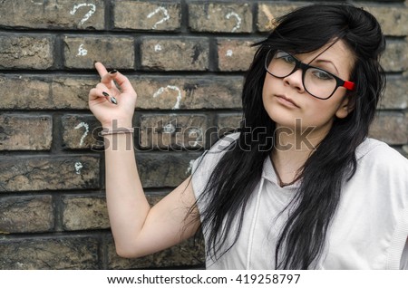 Emo girl with glasses standing outside against a wall with a printed questionnaire