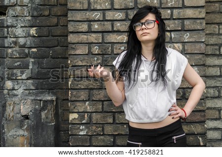 Emo girl with glasses standing outside against a wall with a printed questionnaire