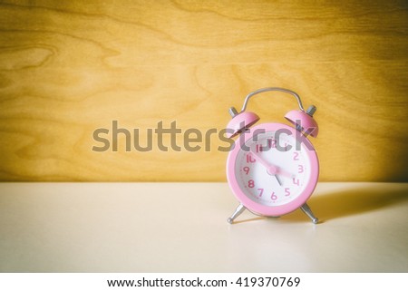 the pink analog alarm clock with the wooden background in vintage style