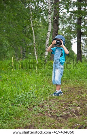 Little boy with a camera shooting outdoor. Kid taking a photo using a digital cam. Green summer  forest glade. Photographing. Happy childhood.