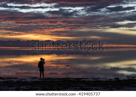 Photographer taking pictures at sunset on beach with colorful and beautiful clouds and reflaction