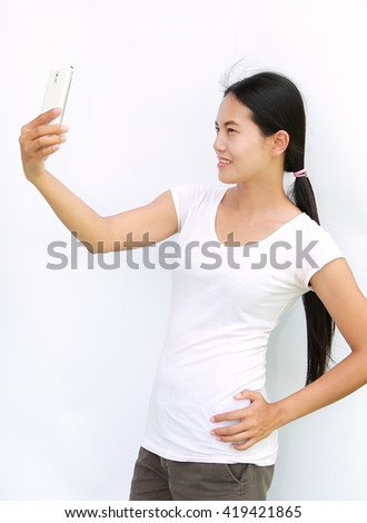 Asian girl taking pictures of herself through cell phone on white background