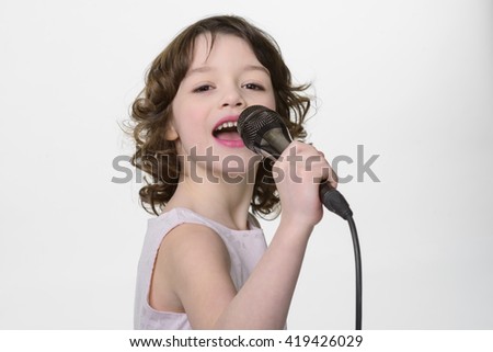 Young singer performs her song. Little girl sings in the microphone she holds in her hands. Opened mouth and fiery eyes while recording her new song in the studio.