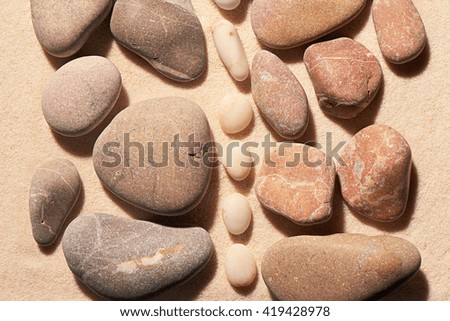 Collections of pink and grey toned sea stones separated by vertical strip of smaller white stones on sand. Summer beach background. View from above