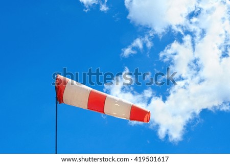 Colorful wind cone with red and white lines flutters on sunny and cloudy day at airfield.