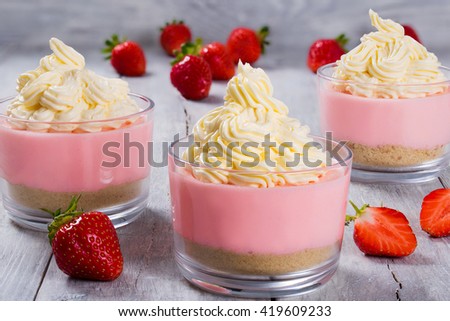 amazing strawberry cheesecake mousse cups decorated by whipped cream on a white wooden table, close-up, macro 