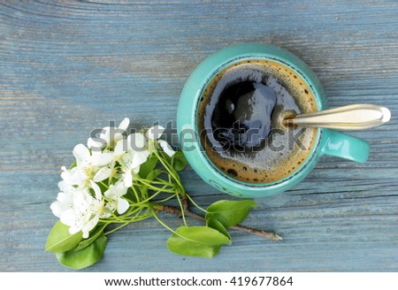 Making coffee in vintage green cup on old withered grunge table with small bunch of white spring flowers. Rustic design. Retro decor elements