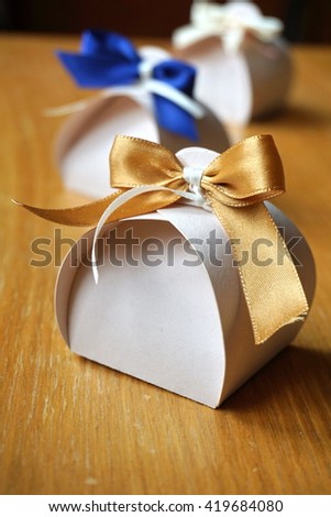 Small gift box made of paper with a colorful ribbon knot atop on a wooden background  