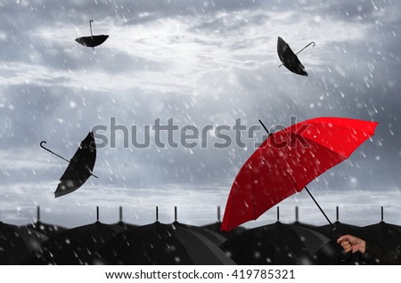 Red umbrella in mass of black umbrellas.