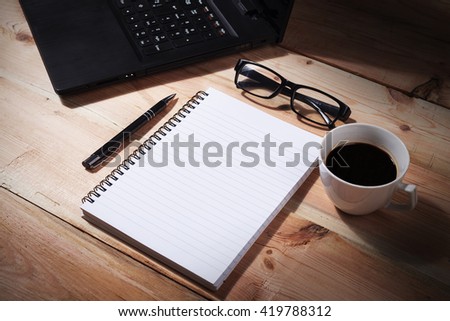 Laptop (notebook) with cup of coffee and notepad with pen on old wooden table.