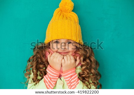 Cute little lady wearing yellow woolen cap and scarf against turquoise background
