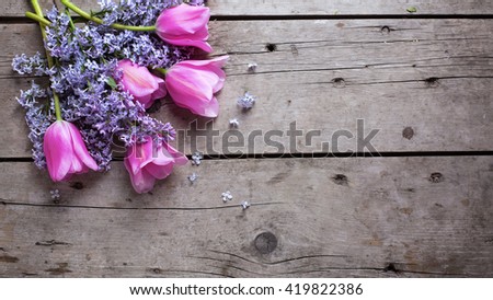 Background with fresh aromatic lilac  and pink tulips flowers on vintage wooden planks. Selective focus. Place for text. Toned image.
