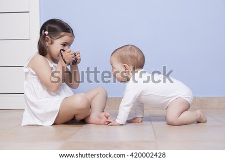 Young girl photographer. Pretty little sister taking pictures to her baby brother with old analog camera