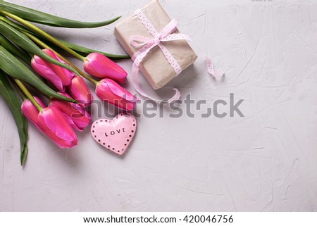Bright pink spring tulips, decorative heart and box with gift  on grey textured background. Selective focus. Place for text. Toned image.