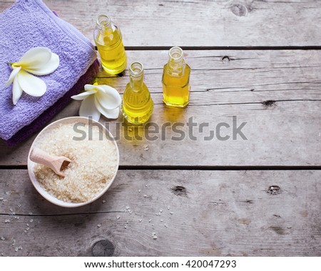 Spa or wellness setting in  yellow and violet colors. Bottles with essential aroma oil, towels, sea salt  on  aged wooden background. Selective focus. Place for text. Top view. Toned image.